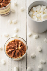 Tiramisu two glasses with marshmallows and a cup of coffee on a light wooden background
