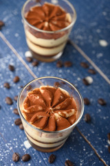 Tiramisu two glasses with coffee grains on a blue wooden background.Vertical photo
