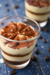 Tiramisu two glasses with coffee grains on a blue wooden background.Vertical photo