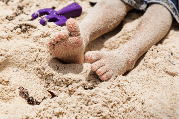 Boy sitting with barefoot on sandy beach, summer vacation concept