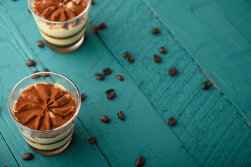 flat lay, Tiramisu two glasses with grains of coffee on a green wooden background.