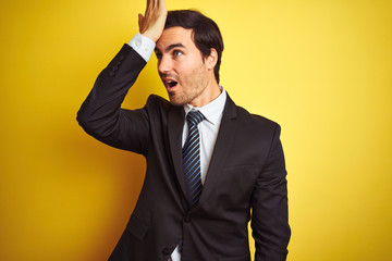 Young handsome businessman wearing suit and tie standing over isolated yellow background surprised...