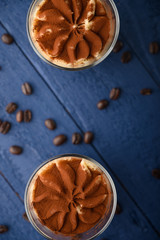 Tiramisu two glasses with coffee grains on a blue wooden background.Vertical photo