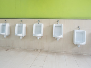 Empty row of outdoor urinals men public toilet and green wall background.Close up different white urinals boy and man in men's toilet.White ceramic urinals for man in lavatory room.Gentlemen restroom 