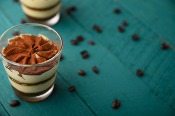 flat lay, Tiramisu two glasses with grains of coffee on a green wooden background.