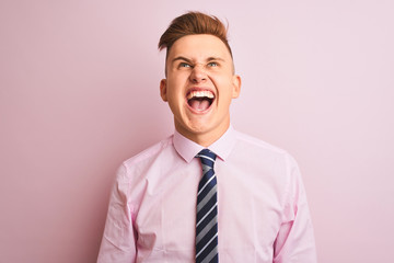 Young handsome businessman wearing shirt and tie standing over isolated pink background angry and mad screaming frustrated and furious, shouting with anger. Rage and aggressive concept.