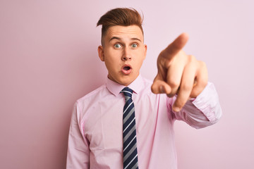 Young handsome businessman wearing shirt and tie standing over isolated pink background Pointing with finger surprised ahead, open mouth amazed expression, something on the front