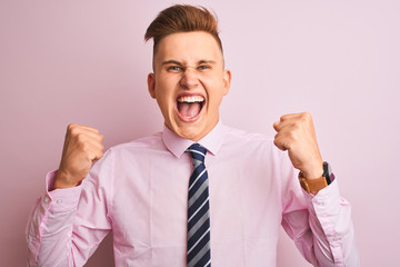 Young handsome businessman wearing shirt and tie standing over isolated pink background very happy and excited doing winner gesture with arms raised, smiling and screaming for success. 