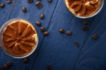 flat lay, Tiramisu two glasses with coffee grains on a blue wooden background. With space for design