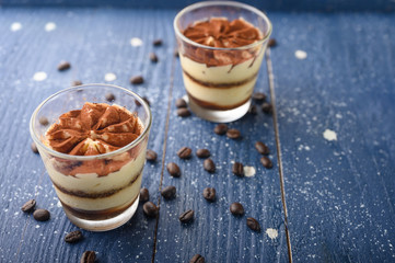 Tiramisu two glasses with coffee grains on a blue wooden background. With space for design