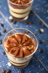 Tiramisu two glasses with coffee grains on a blue wooden background.Vertical photo