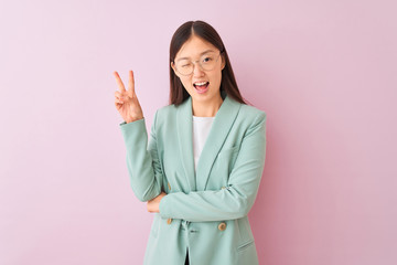 Young chinese businesswoman wearing jacket and glasses over isolated pink background smiling with happy face winking at the camera doing victory sign. Number two.