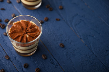 flat lay, Tiramisu two glasses with coffee grains on a blue wooden background. With space for design