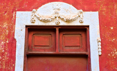 Old red portal with relief decorations, architecture detail in an old romantic Latino district.