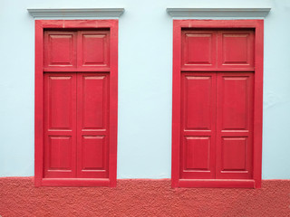 Two burgundy red closed windows and a pale blue wall, small town architecture detail.