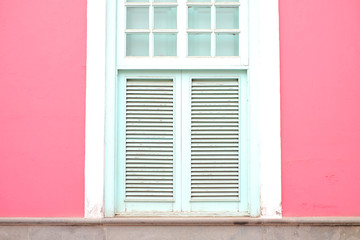 Fototapeta na wymiar Pale pink wall and white wooden frame window with venetian blinds.