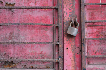 Old red rusty metal door barred and closed with a rusty padlock, a bankrupt small business.
