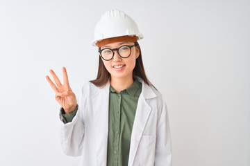 Young chinese engineer woman wearing coat helmet glasses over isolated white background showing and pointing up with fingers number three while smiling confident and happy.