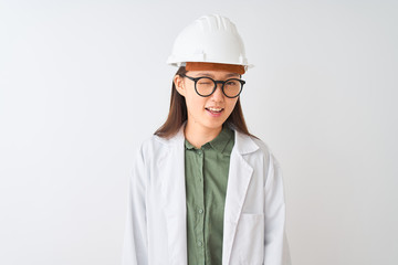 Young chinese engineer woman wearing coat helmet glasses over isolated white background winking looking at the camera with sexy expression, cheerful and happy face.