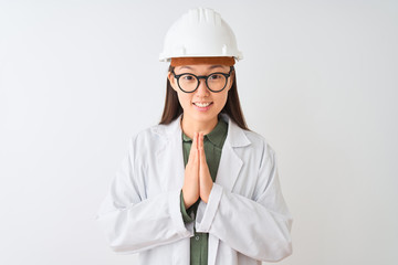Young chinese engineer woman wearing coat helmet glasses over isolated white background praying with hands together asking for forgiveness smiling confident.