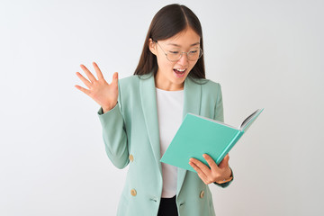 Young chinese student woman wearing glasses reading book over isolated white background very happy and excited, winner expression celebrating victory screaming with big smile and raised hands