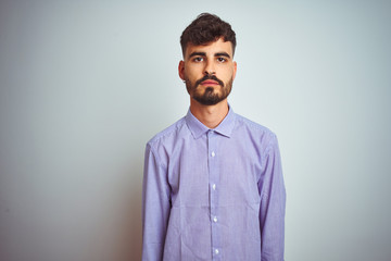 Obraz premium Young man with tattoo wearing purple shirt standing over isolated white background with serious expression on face. Simple and natural looking at the camera.