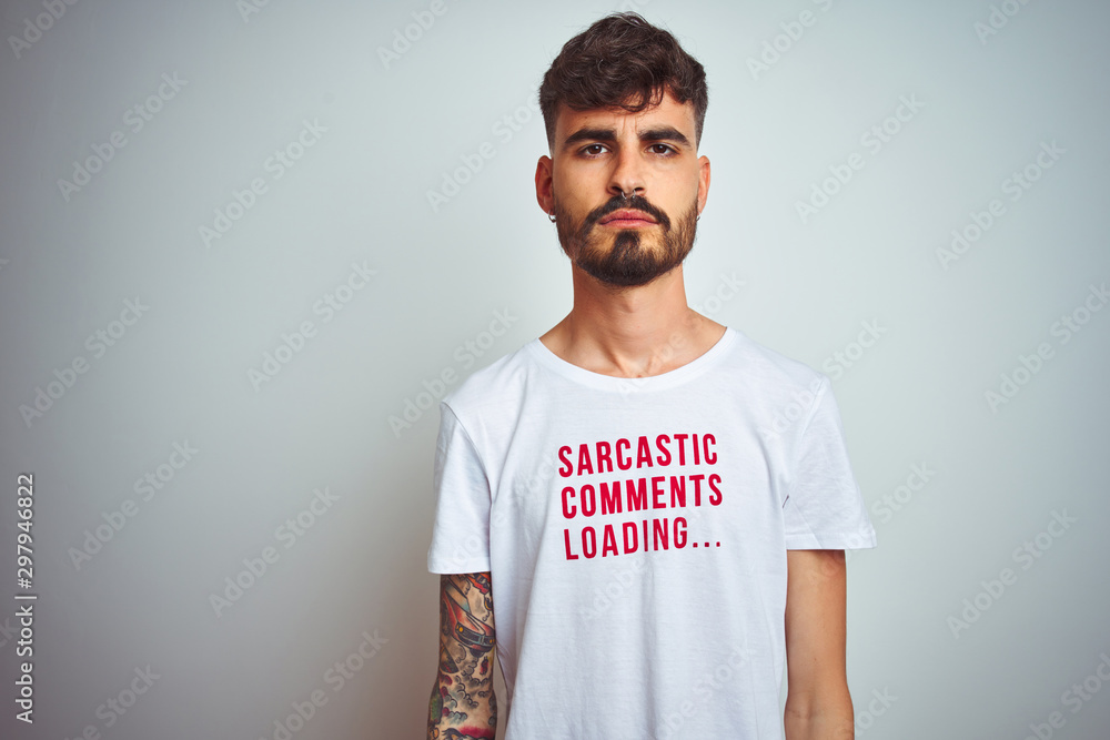 Sticker young man with tattoo wearing fanny t-shirt standing over isolated white background with serious exp