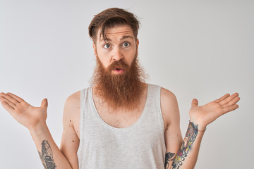 Young redhead irish man wearing t-shirt standing over isolated grey background clueless and...