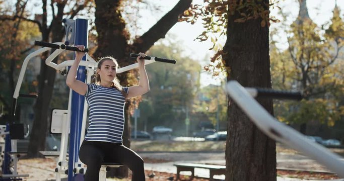Teenager girl is engaged on a simulator, practicing fitness in park.
