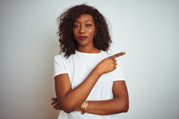 Young african american woman wearing t-shirt standing over isolated white background Pointing with hand finger to the side showing advertisement, serious and calm face