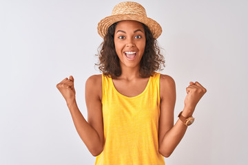 Obraz na płótnie Canvas Young brazilian woman wearing yellow t-shirt and summer hat over isolated white background celebrating surprised and amazed for success with arms raised and open eyes. Winner concept.