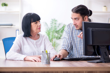 Young male employee explaining to old female colleague how to us