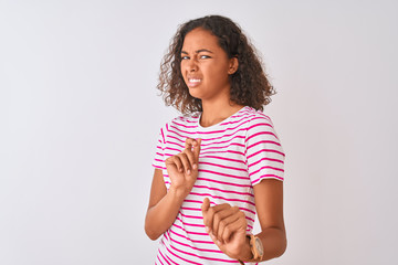 Young brazilian woman wearing pink striped t-shirt standing over isolated white background disgusted expression, displeased and fearful doing disgust face because aversion reaction. With hands raised