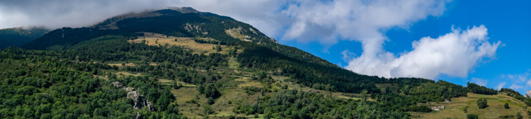 Obraz premium Mountain landscape in Setcasas, Catalunya, Spain. Mountain covered with green trees and shrubs on cloudy blue sky background. Panoramic view, natural background.