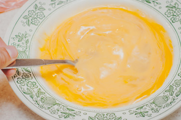 Beating eggs in a white plate with a fork. Cooking morning omelet. Homogeneous mass.