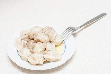 A small portion of freshly cooked dumplings with butter sprinkled with pepper on a white plate with a fork.