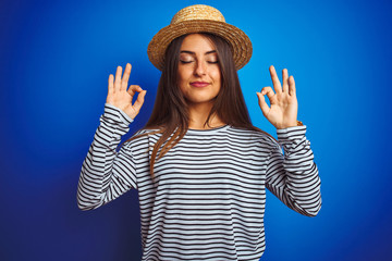 Young beautiful woman wearing navy striped t-shirt and hat over isolated blue background relax and...