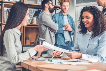 Startupers working together at office women sitting at table passing documents joyful