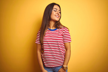 Obraz premium Young beautiful woman wearing striped t-shirt standing over isolated yellow background looking away to side with smile on face, natural expression. Laughing confident.