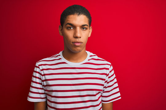 Young handsome arab man wearing striped t-shirt over isolated red background Relaxed with serious expression on face. Simple and natural looking at the camera.