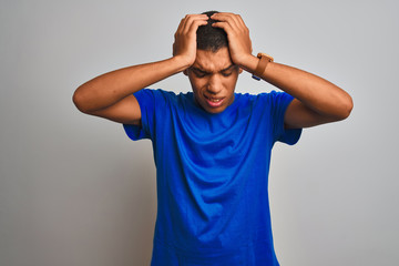 Young handsome arab man wearing blue t-shirt standing over isolated white background suffering from headache desperate and stressed because pain and migraine. Hands on head.