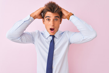 Young handsome businessman wearing shirt and tie standing over isolated pink background Crazy and scared with hands on head, afraid and surprised of shock with open mouth