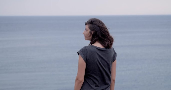 Girl standing on a cliff and looking into sea, slow motion