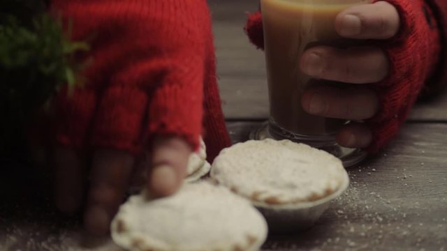 Hand wearing winter gloves grabbing pies and coffee in Christmas background