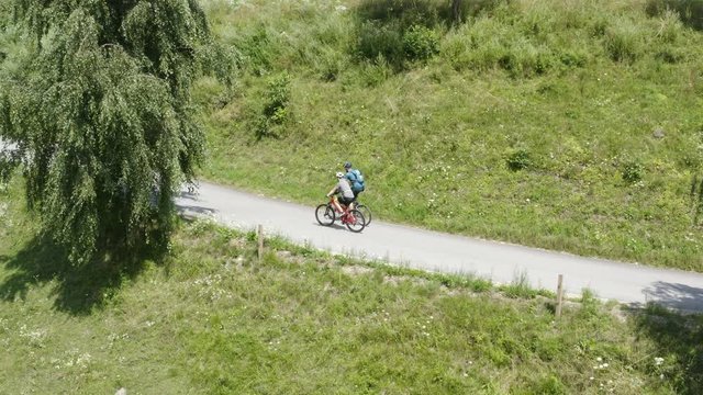 Aerial sideways tracking shot of two people riding bicycles on the country road on a sunny day in Prevalje, Slovenia