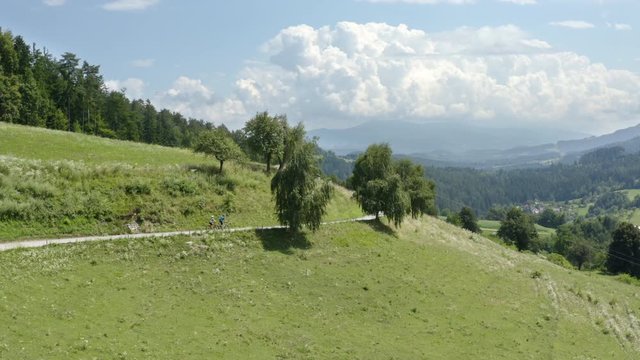 Aerial of two people riding bicycles on a mountain country road in nature in Prevalje Slovenia, lateral tracking shot