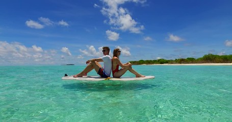 A couple sitting on a white paddle board near a beach along the island of Hawaii
