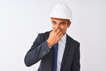 Young handsome architect man wearing suit and helmet over isolated white background smelling...
