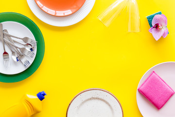 Washing dishes frame with plates, sponges, dishwashing liquid on yellow background top view space for text