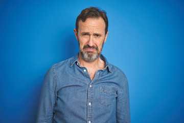 Fototapeta premium Handsome middle age senior man with grey hair over isolated blue background depressed and worry for distress, crying angry and afraid. Sad expression.